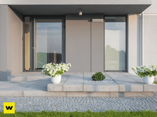 Moderner Hauseingang mit grauen Fliesen, weißen Blumentöpfen und dekorativem Kiesbeet.