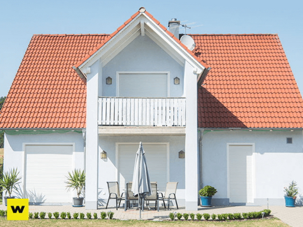 Modernes Einfamilienhaus mit rotem Satteldach, Balkon und Terrasse bei sonnigem Wetter.